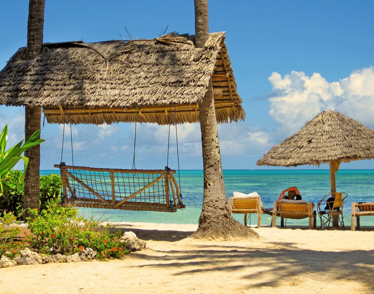 Thatched beach hut and hammock swing on a Zanzibar white-sand beach with turquoise water